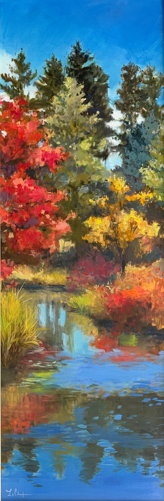 A tall narrow view of autumn woodland, scarlet and gold trees banked against dark evergreens above still water that holds their reflection. Oil painting by Lorraine Skelskey-Chapin, 30 by 10 inches.